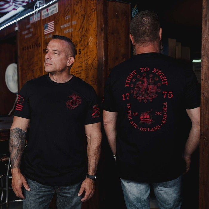 Two men wearing black t-shirts with red text and graphics, standing in a bar setting.