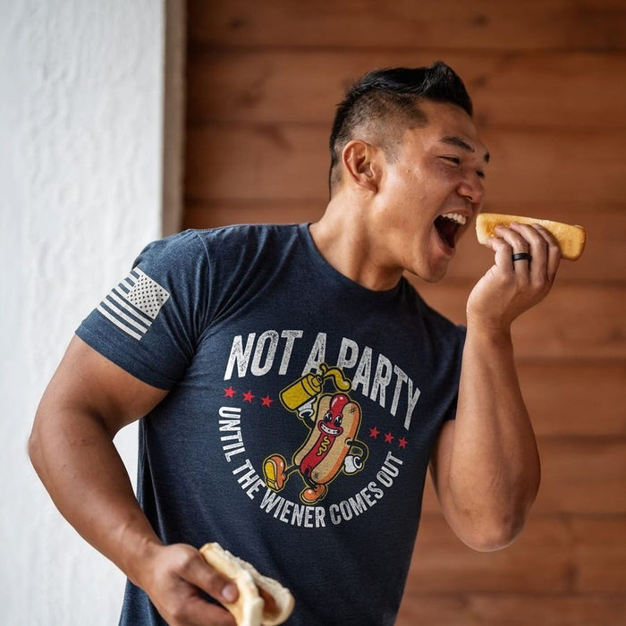 Man eating a hot dog wearing a t-shirt with a humorous graphic and text.