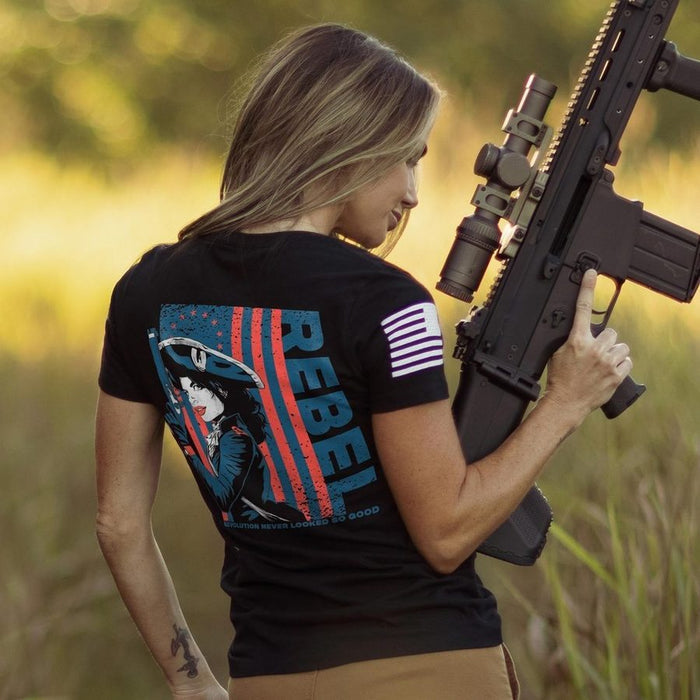 Person wearing a black t-shirt with a graphic design and text, holding a rifle in an outdoor setting.