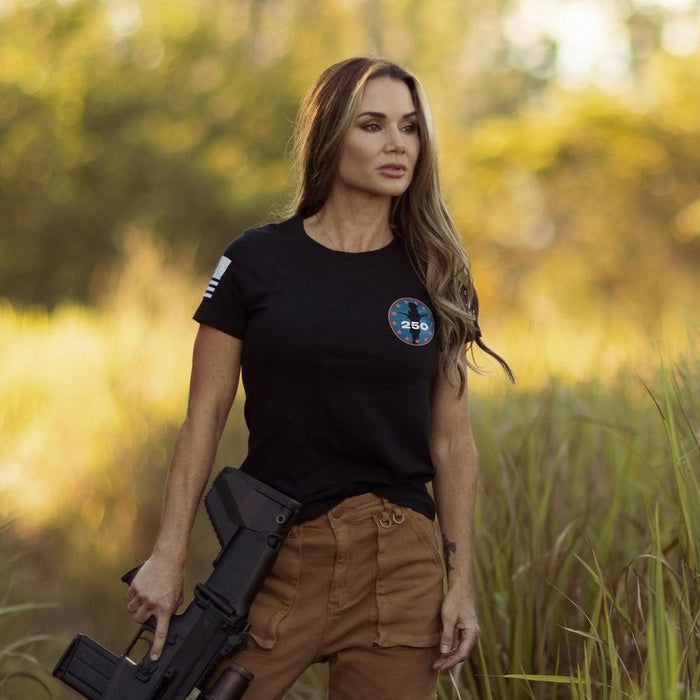 Woman holding a rifle in a natural setting with greenery