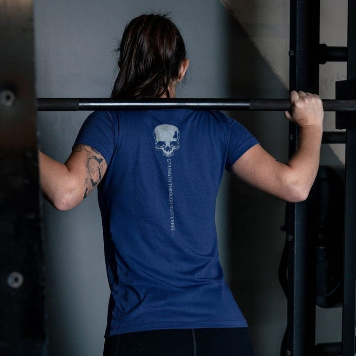 Person wearing a blue t-shirt with a skull design, lifting a barbell in a gym setting.