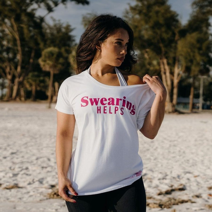 Woman wearing a white t-shirt with 'Swearing Helps' text on a beach.